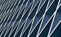An abstract, close-up shot of a modern architectural facade featuring a diagonal lattice of silver or white metal beams over deep blue panels.