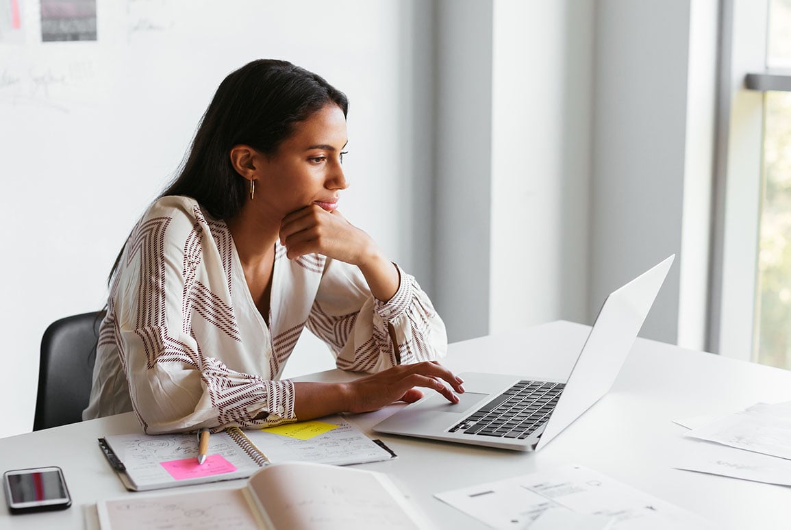 image of woman doing research on a laptop with notepad next to her