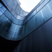 Low-angle perspective of a modern curved building exterior featuring vertical ribbed panels and glass windows.