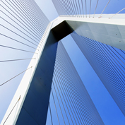 Low-angle view looking up at a modern white cable-stayed bridge pylon and fan-patterned steel cables against a clear blue sky, symbolizing strength and structural resilience.