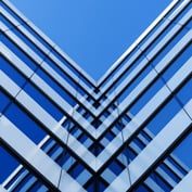 An abstract architectural photograph featuring symmetrical blue and white geometric lines converging in a V-shape against a clear blue sky, representing stability and structure.