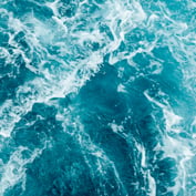 Top-down view of turbulent, deep teal ocean water with white foam and swirling waves.