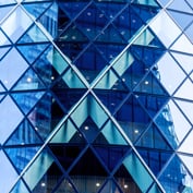 A close-up of a modern glass skyscraper facade featuring a structured, repeating geometric pattern of blue and teal triangular windows.