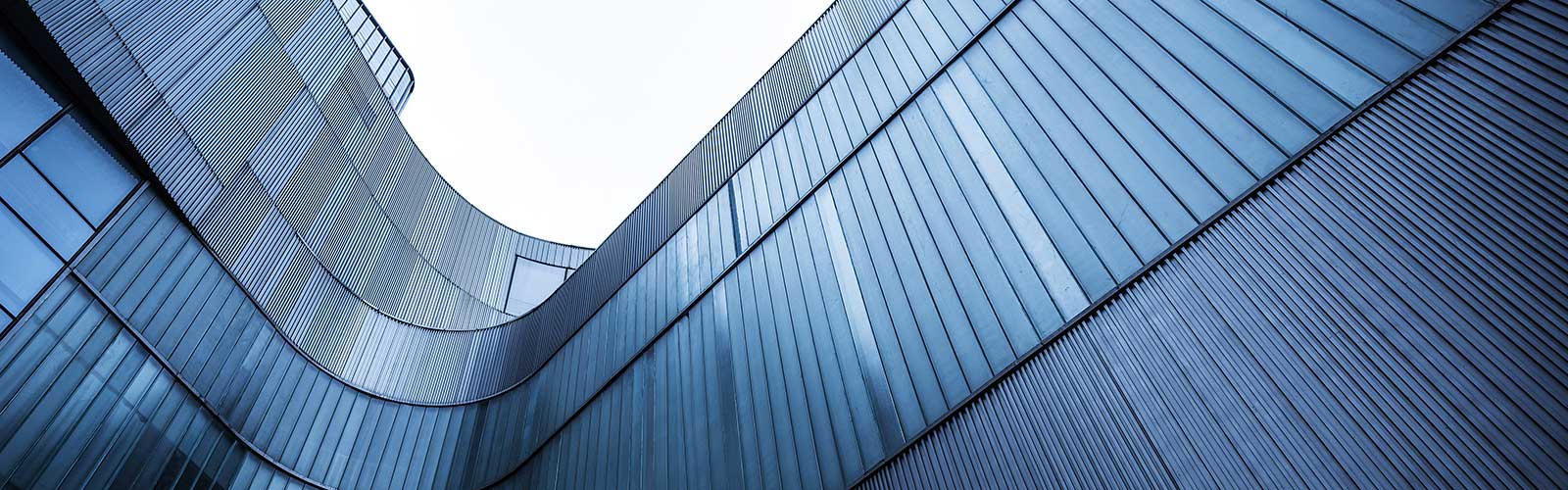 Low-angle perspective of a modern curved building exterior featuring vertical ribbed panels and glass windows.