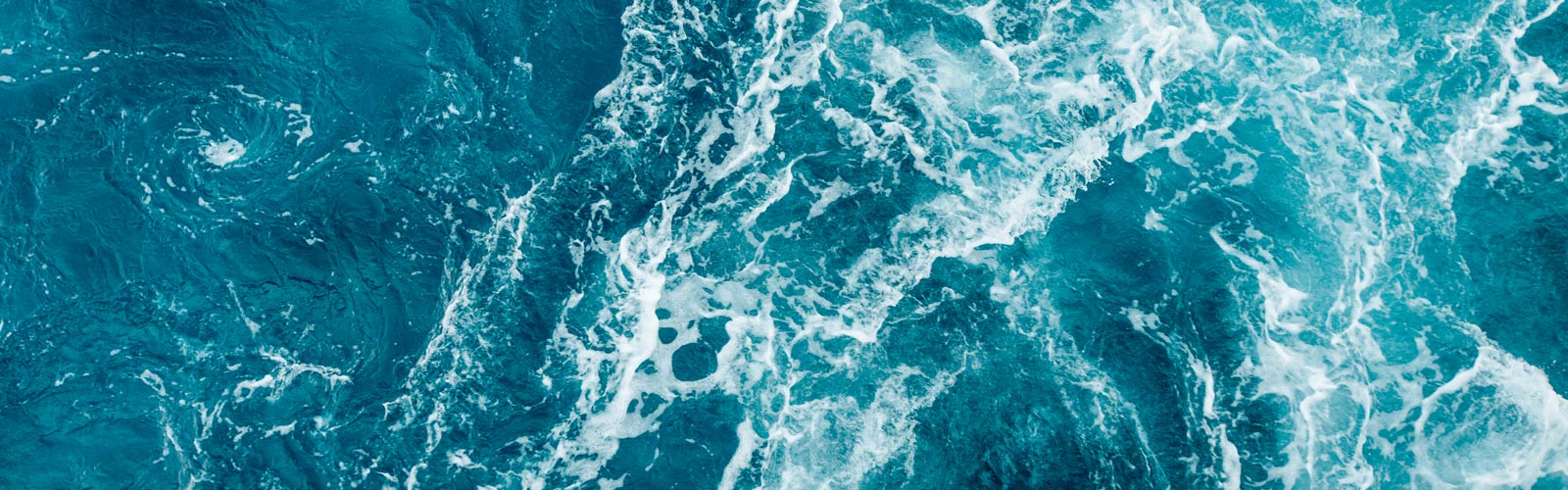 Top-down view of turbulent, deep teal ocean water with white foam and swirling waves.