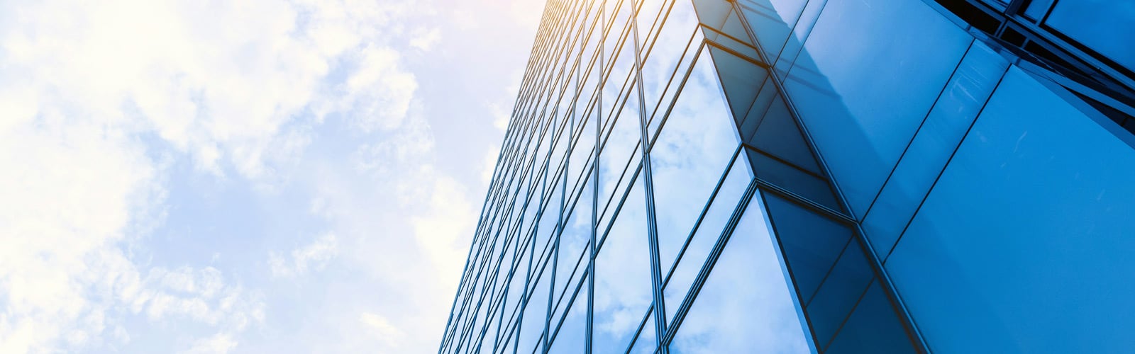 A modern glass office building towers against a partly cloudy sky, with sunlight gleaming off its blue windows.