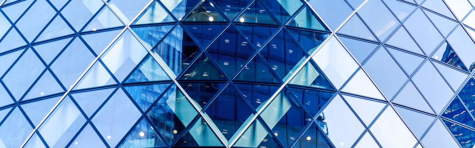 A close-up of a modern glass skyscraper facade featuring a structured, repeating geometric pattern of blue and teal triangular windows.