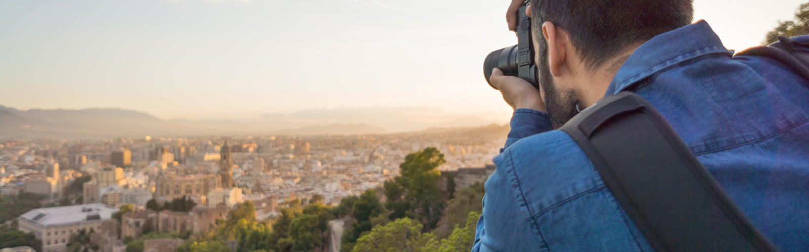 Person photographing a city and mountains at sunset.