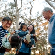 An intergenerational family joyfully plays together outdoors.