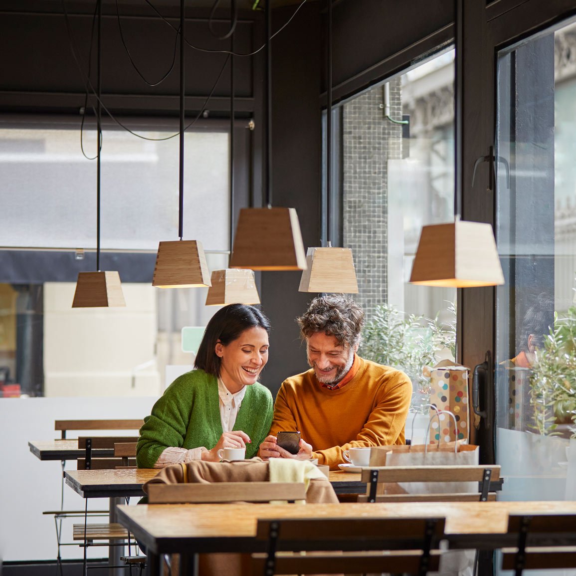 Middle aged man and woman sitting in coffee shop smiling at a phone